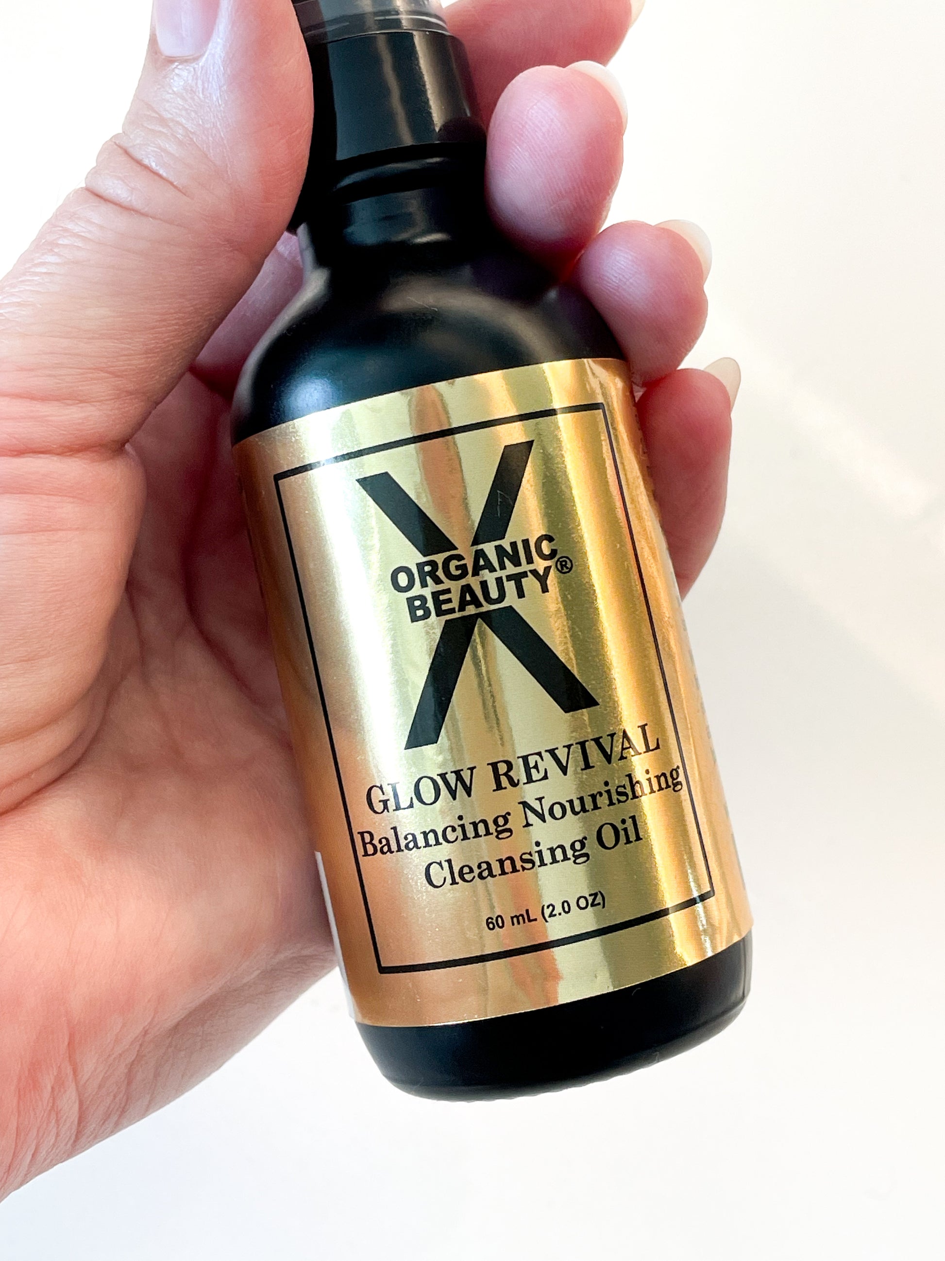 Hand holding a bottle of Organic Glow Revival Cleansing Oil against a white background
