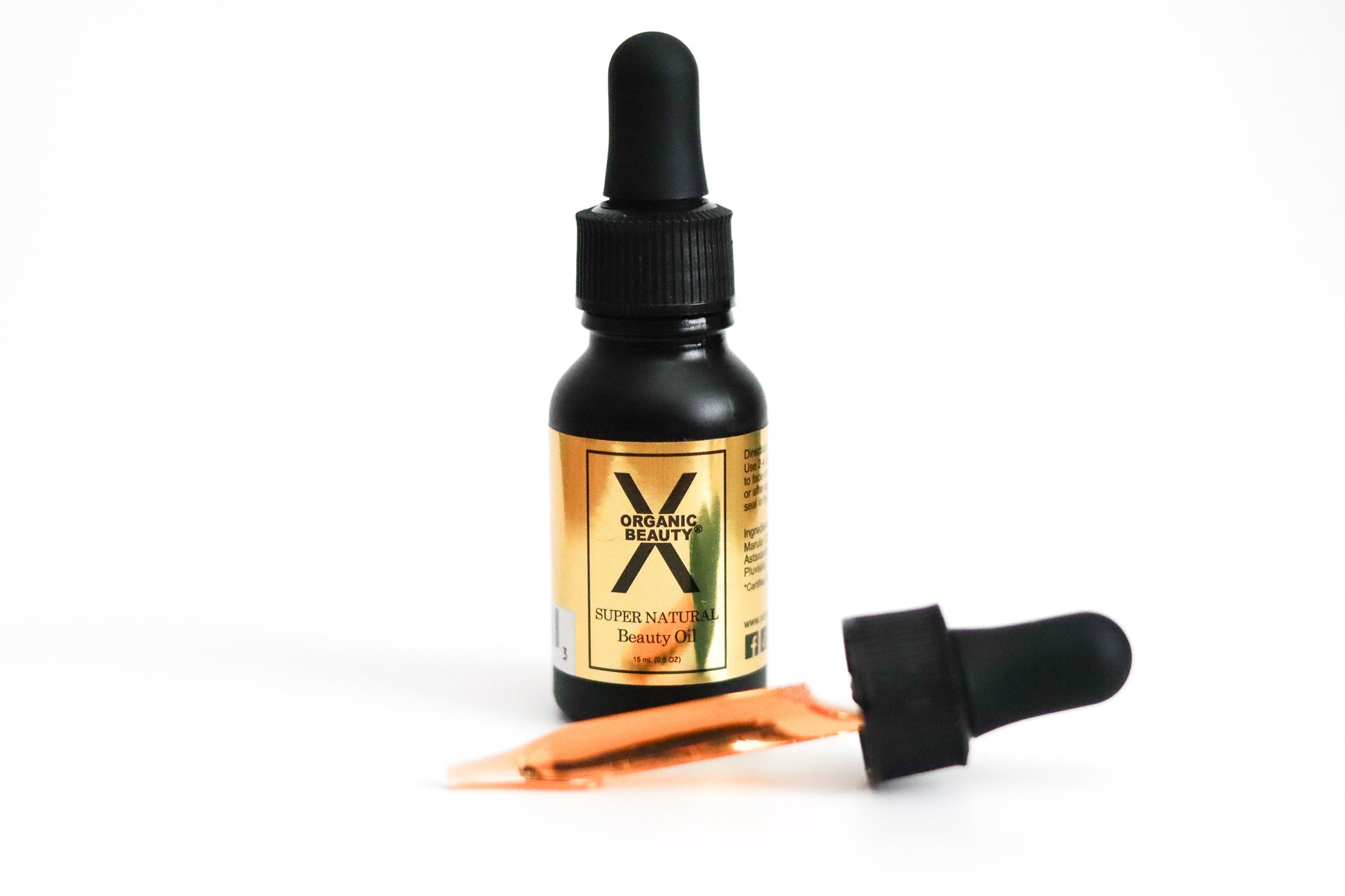 A half ounce bottle of Super Natural Beauty Oil with a dropper full of the orange fluid on a white background