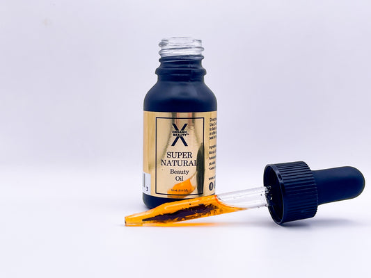 A front view of a bottle of Super Natural Beauty Oil with the dropper top in front of the bottle, on it's side, filled with the orange/red oil.